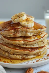 Fluffy banana oatmeal pancakes topped with syrup and fresh bananas